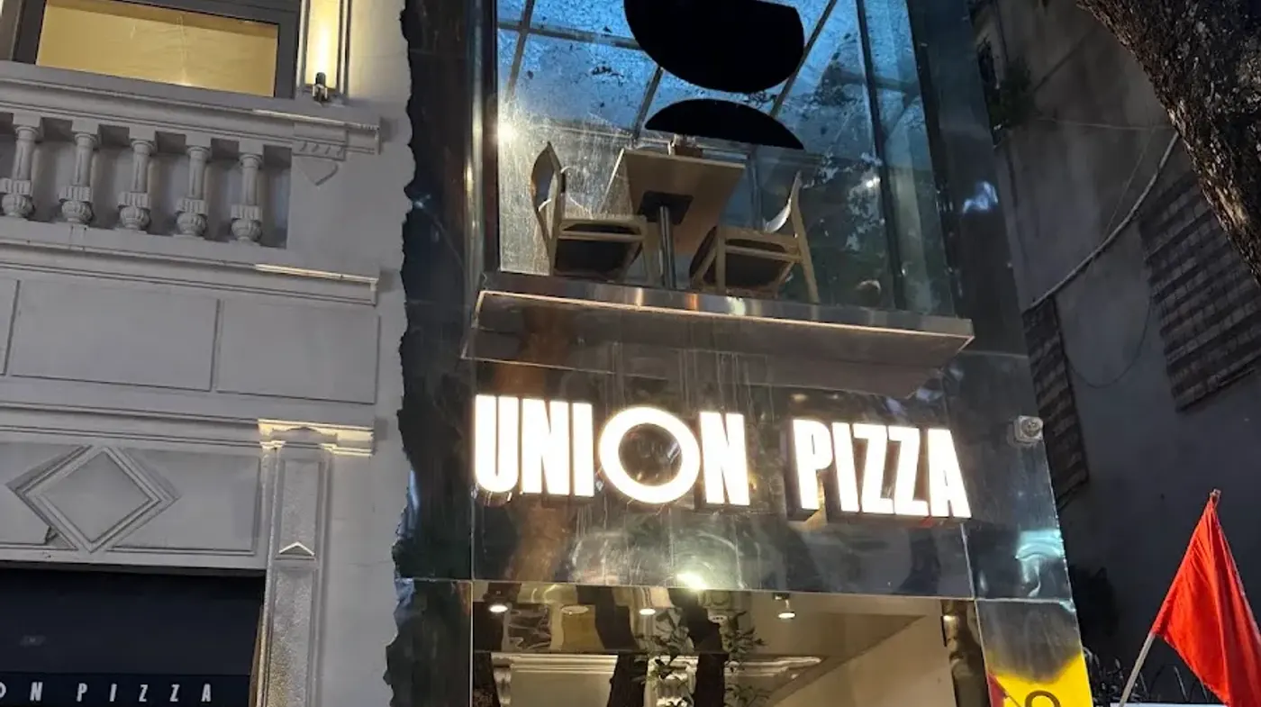 Mặt tiền thép gương Union Pizza lên đèn neon buổi tối, soi bóng hàng cây phố Phan Đình Phùng